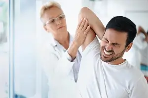 older blond female medical professional checking out shoulder range of movement on young male patient