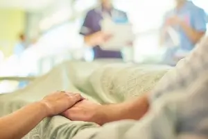close up of family member holding hands of a patient ready to go to surgery. Medical professionals blurred in background